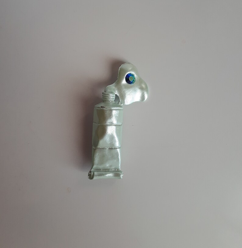 May include: A silver paint tube with a blue and green jewel on the cap.