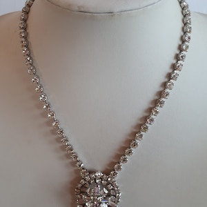 Può includere: Una collana d'argento con un ciondolo di cristallo e orecchini di cristallo abbinati. Il ciondolo è un gruppo di cristalli a forma di lacrima con un gruppo più piccolo di cristalli che pendono dalla parte inferiore.