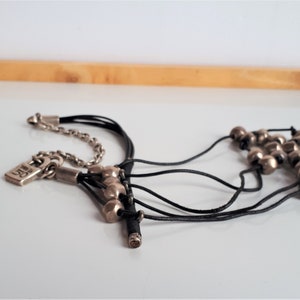 Pode incluir: Um colar de v&aacute;rias voltas com um fecho de prata e contas de prata. O colar &eacute; feito de cord&atilde;o de couro preto e tem um fecho de prata.