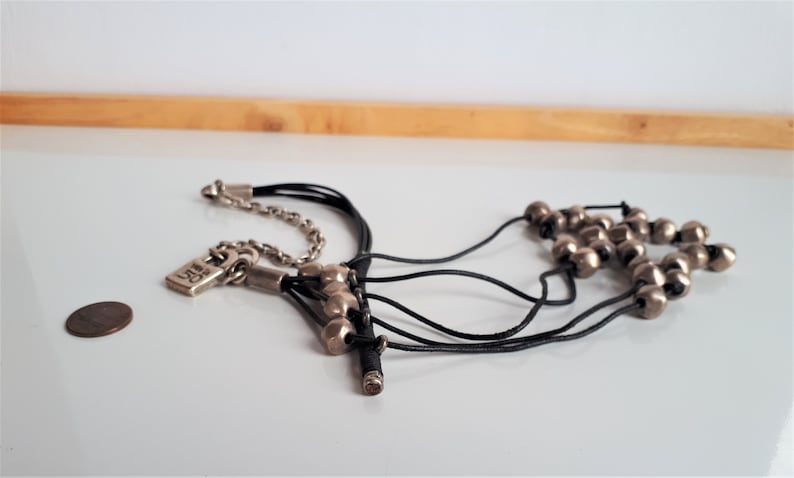 Pode incluir: Um colar de v&aacute;rias voltas com um fecho de prata e contas de prata. O colar &eacute; feito de cord&atilde;o de couro preto e tem um fecho de prata.