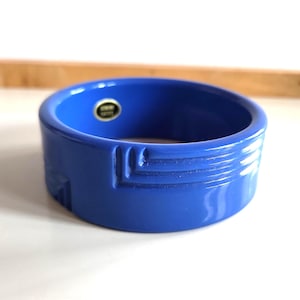 Puede incluir: Un brazalete azul vibrante y ancho. El brazalete presenta un diseño geométrico con líneas grabadas y un acabado brillante. Una pequeña pegatina es visible en el interior. Un accesorio llamativo y moderno.