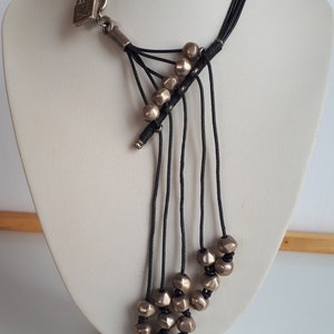 Pode incluir: Um colar longo de cord&atilde;o preto com contas prateadas. O colar tem um fecho de cadeado prateado e v&aacute;rias cordas.