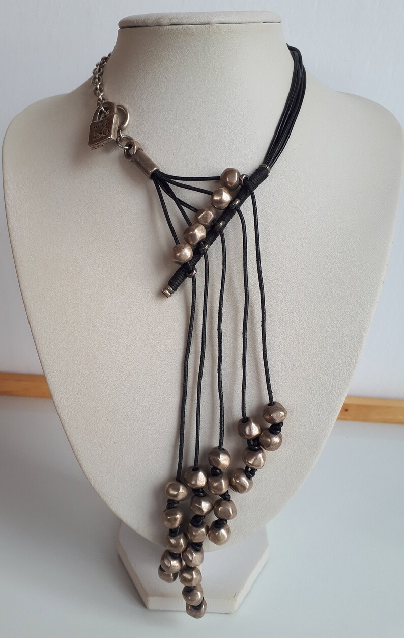 Pode incluir: Um colar longo de cord&atilde;o preto com contas prateadas. O colar tem um fecho de cadeado prateado e v&aacute;rias cordas.