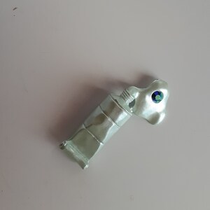 May include: A light green paint tube with a blue and green jewel on the cap.