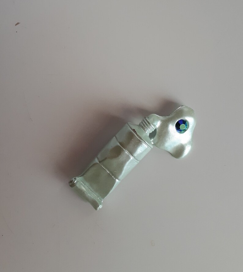 May include: A light green paint tube with a blue and green jewel on the cap.