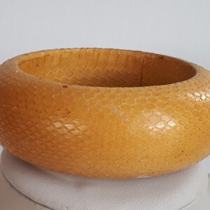 Puede incluir: Un brazalete de cuero amarillo con un patrón texturizado de piel de serpiente.