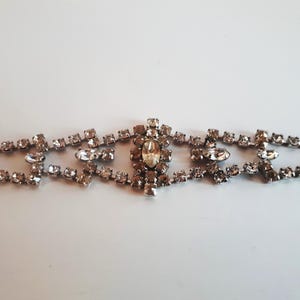 Può includere: Un braccialetto in argento con strass, con un grande strass trasparente al centro. Il braccialetto è realizzato con piccoli strass trasparenti incastonati in un metallo argentato.