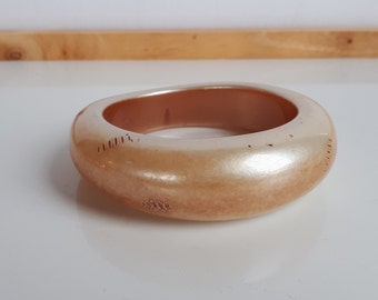 May include: A large, off-white bangle bracelet with a pearlescent finish. The bracelet has a smooth, rounded shape and a subtle, textured surface.