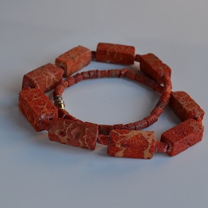 Puede incluir: Un collar de coral rojo con cuentas rectangulares. Las cuentas tienen una superficie rugosa y texturizada y están conectadas por un cordón delgado de plata.