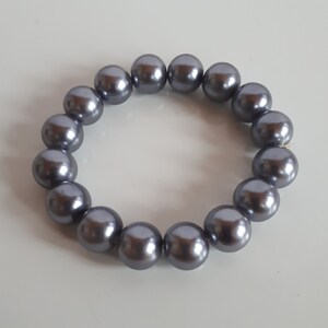 May include: A gray pearl bracelet with a simple design. The bracelet is made of round, smooth pearls that are strung together on a clear elastic cord.