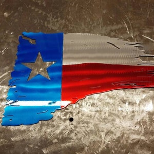 May include: A distressed metal Texas flag wall decor with a blue, white, and red color scheme. The flag is shaped like a tattered banner with a white star in the blue section.