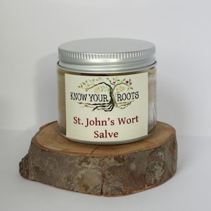 May include: A small glass jar with a silver lid, containing a yellow salve. The jar has a white label with the text "KNOW YOUR ROOTS" and "St. John's Wort Salve" in red and black lettering.