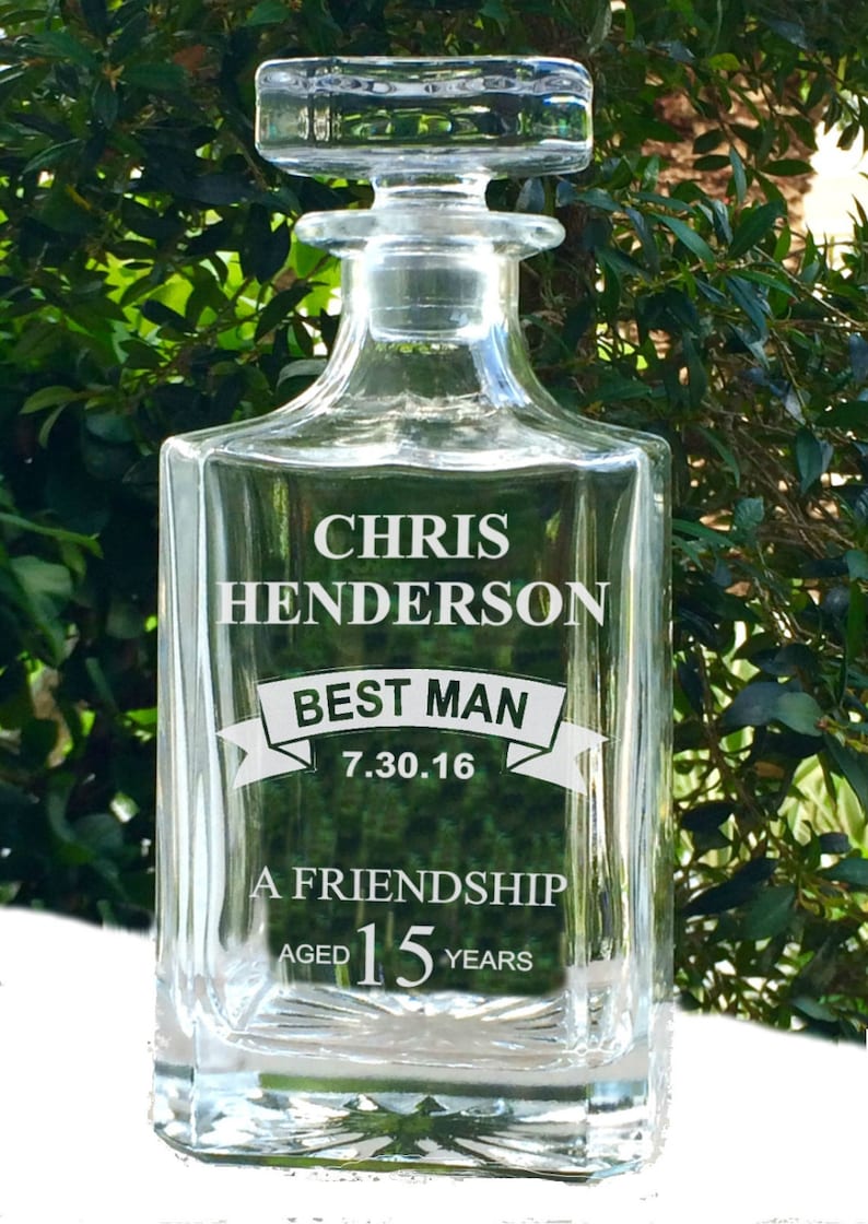 May include: A clear glass decanter with a square base and a stopper. The front of the decanter is engraved with the name "CHRIS HENDERSON", the words "BEST MAN", the date "7.30.16", and the phrase "A FRIENDSHIP AGED 15 YEARS".