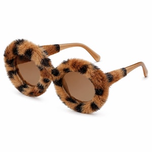 Pode incluir: Óculos de sol redondos com uma armação texturizada e felpuda com estampa de leopardo em tons de castanho e preto. As lentes circulares são tingidas de castanho e as hastes são de plástico liso e sólido na cor bege.