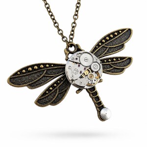 May include: A dragonfly pendant necklace featuring a bronze-toned metal body with textured wings and a circular watch movement mechanism as the thorax. The piece includes a matching bronze chain and a small silver-toned gear at the tail end.
