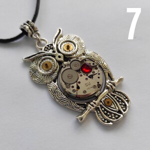 May include: Silver-toned owl pendant necklace with intricate details. The owl's body features a watch mechanism with visible gears and a red jewel. The pendant hangs from a black cord, creating a unique steampunk accessory.
