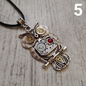 May include: Silver-toned owl pendant necklace with a steampunk design. The owl features intricate gear details, a red jewel, and a black cord. The pendant is approximately 2 inches in height.