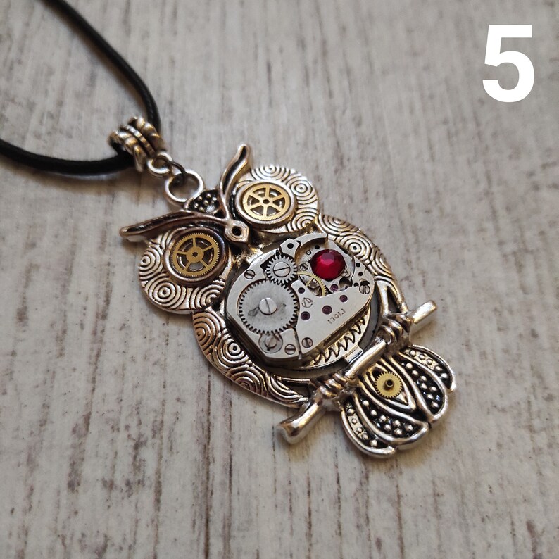 May include: Silver-toned owl pendant necklace with a steampunk design. The owl features intricate gear details, a red jewel, and a black cord. The pendant is approximately 2 inches in height.