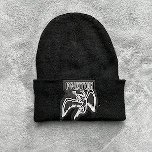 May include: Black knit beanie with a white embroidered Led Zeppelin logo featuring a winged creature.
