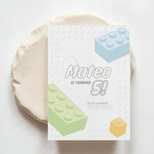 Puede incluir: Una tarjeta de invitación blanca con un diseño de bloques de Lego azul claro y verde. El texto en la tarjeta dice "Mateo cumple 5!"