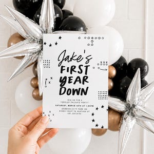May include: A white rectangular invitation card with black text reading Jake's FIRST YEAR DOWN, Join us for a toddler tailgate party, Saturday, March 10th at 1:00pm, Edmonds City Park WA, Kindly RSVP to Heather at 301.220.0133, with star and dot graphics.