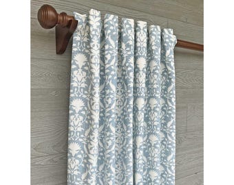 May include: A light blue and white curtain panel featuring a repeating floral and vine pattern. The fabric is hung on a dark brown wooden curtain rod with decorative finials. The text "Fabric: Peacefulness in Luna" is visible at the bottom.
