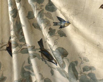 May include: A cream-colored fabric featuring a repeating pattern of small birds perched on branches with muted green leaves. The birds are depicted in shades of blue, brown, and tan, with soft, flowing folds in the material creating depth and texture.