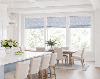 May include: Three light blue and white patterned fabric roman shades installed on a set of large windows in a dining area. The shades feature a repeating floral or botanical print and are shown in a partially raised position with soft folds.