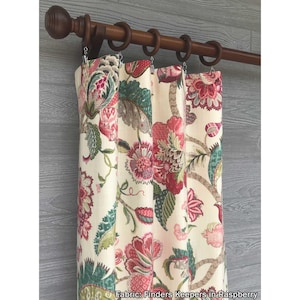 May include: A curtain panel featuring a cream background with a floral pattern in shades of red, pink, and green. The fabric is suspended from a dark brown wooden rod with matching rings. The text Fabric: Finders Keepers in Raspberry is visible.