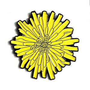 May include: Yellow enamel pin of a stylized flower with black outlines. The pin is on a white card with the text "blond eyed girl" in black.