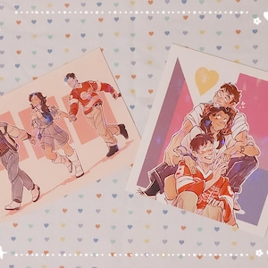 Puede incluir: Dos impresiones artísticas con ilustraciones de personas. Una muestra tres figuras tomadas de la mano y caminando. La otra representa a un grupo de personas en un abrazo cercano. Las impresiones están sobre un fondo estampado.