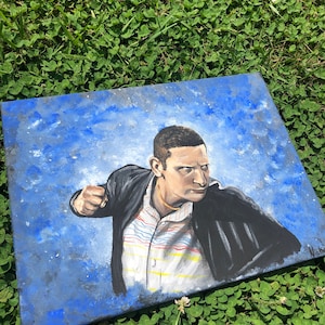 May include: A painting on canvas of a man in a black jacket and a striped shirt, with a blue background. The man is looking to the right and has a serious expression on his face.