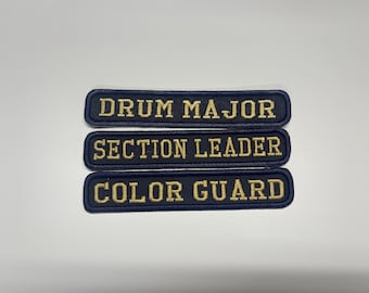 Könnte beinhalten: Drei rechteckige bestickte Aufnäher mit dunkelblauem Stoff und goldener Schrift. Der oberste Aufnäher zeigt DRUM MAJOR, der mittlere SECTION LEADER und der untere COLOR GUARD. Jeder Aufnäher hat einen dunkelblau gestickten Rand.