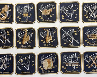 Könnte beinhalten: Ein Set aus fünfzehn quadratischen Stickaufnähern auf weißem Hintergrund. Jeder dunkelblaue Aufnäher zeigt ein gold umrandetes Musikinstrument oder Marschband-Equipment, ein weißes Dreieck, Noten und den Namen in goldener Schrift.