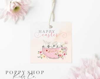 Könnte beinhalten: Rosafarbener Geschenkanhänger mit dem Text "Happy easter" in Kursivschrift. Drei weiße Kaninchen sitzen in einer rosa Teetasse mit weißen Punkten. Die Teetasse ist von rosa und weißen Blumen umgeben. Der Anhänger ist mit einer weißen Schnur gebunden.