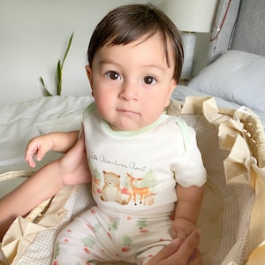 Puede incluir: Un body de beb&eacute; de manga corta en color crema con ribete verde claro, con un estampado de acuarela de un oso, un ciervo y un zorro con setas y el texto Little Adventures Await, combinado con pantalones a juego con un estampado de bosque.