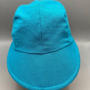 May include: A turquoise baseball cap with a curved brim. The cap is made of a textured fabric and has a classic six-panel design. The brim is a solid color, and the cap appears to be unworn.
