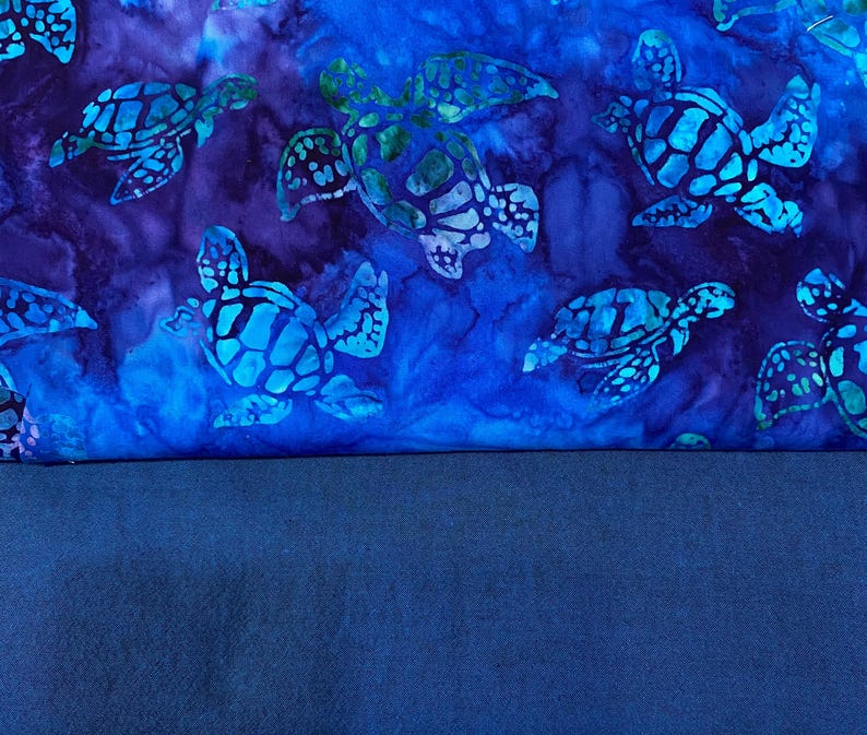May include: A fabric design featuring sea turtles in shades of blue and green against a dark blue and purple background. The turtles have detailed patterns on their shells. The lower portion of the image is a solid, dark blue fabric.