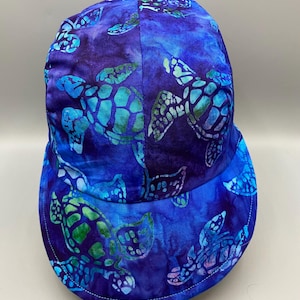 May include: A blue baseball cap with a sea turtle pattern. The cap features a vibrant design of sea turtles in shades of blue and green against a dark blue background. The cap has a curved brim and a stitched edge.