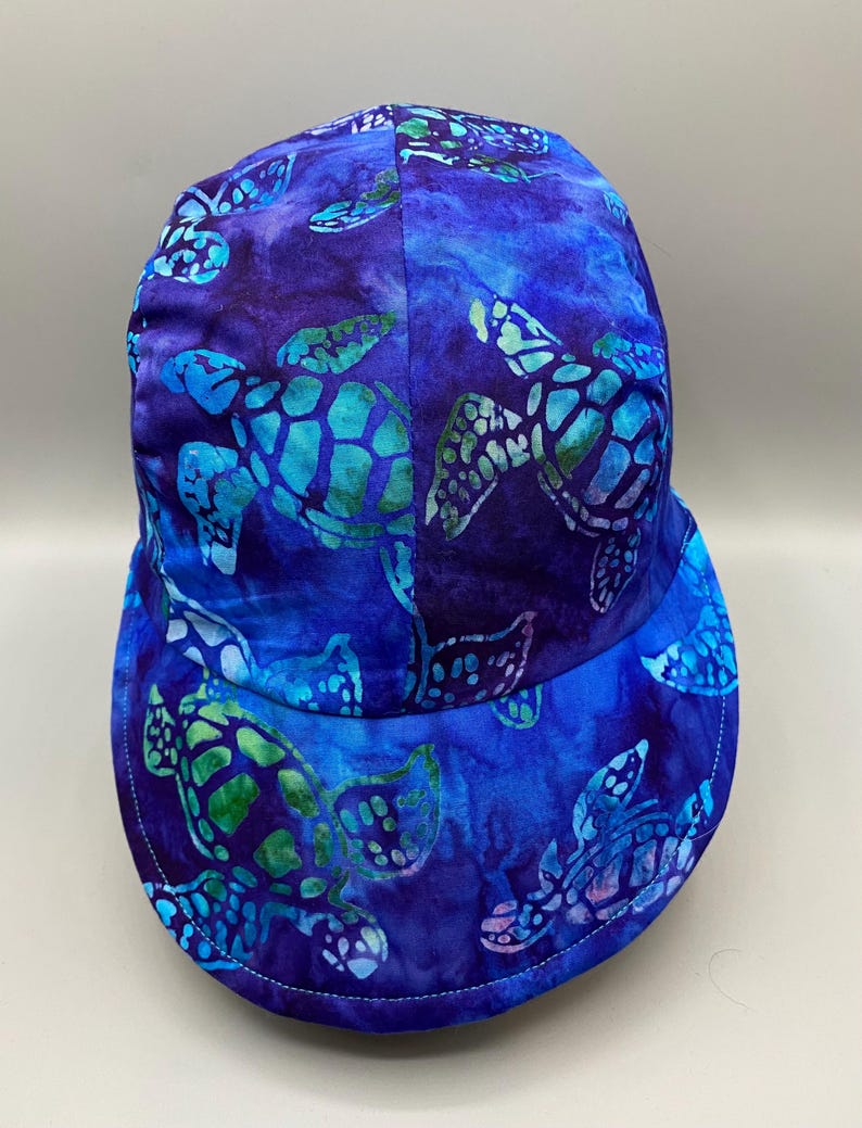 May include: A blue baseball cap with a sea turtle pattern. The cap features a vibrant design of sea turtles in shades of blue and green against a dark blue background. The cap has a curved brim and a stitched edge.