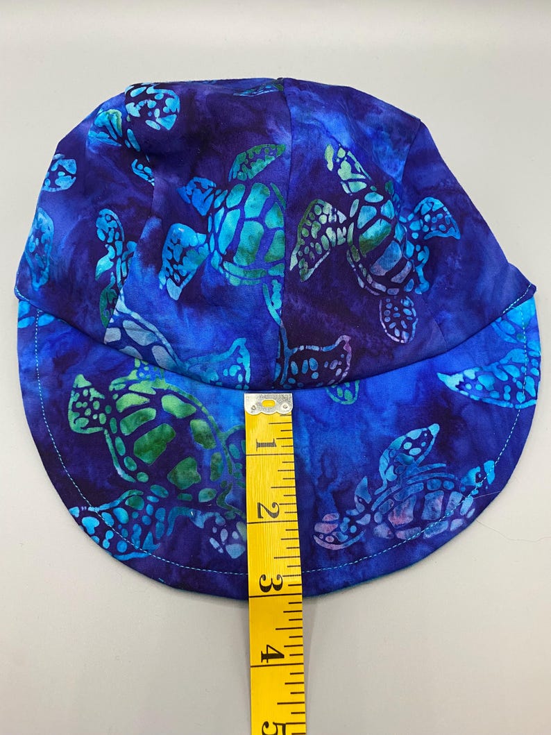 May include: A blue fabric hat with a pattern of sea turtles in shades of blue and green. The hat is approximately 5 inches in height. The hat has a curved brim and is made of a soft fabric.