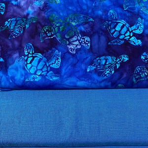 May include: A fabric with a blue and teal sea turtle pattern. The turtles have a detailed shell design and are set against a dark blue background with lighter blue accents. The bottom portion of the image is a solid blue fabric.