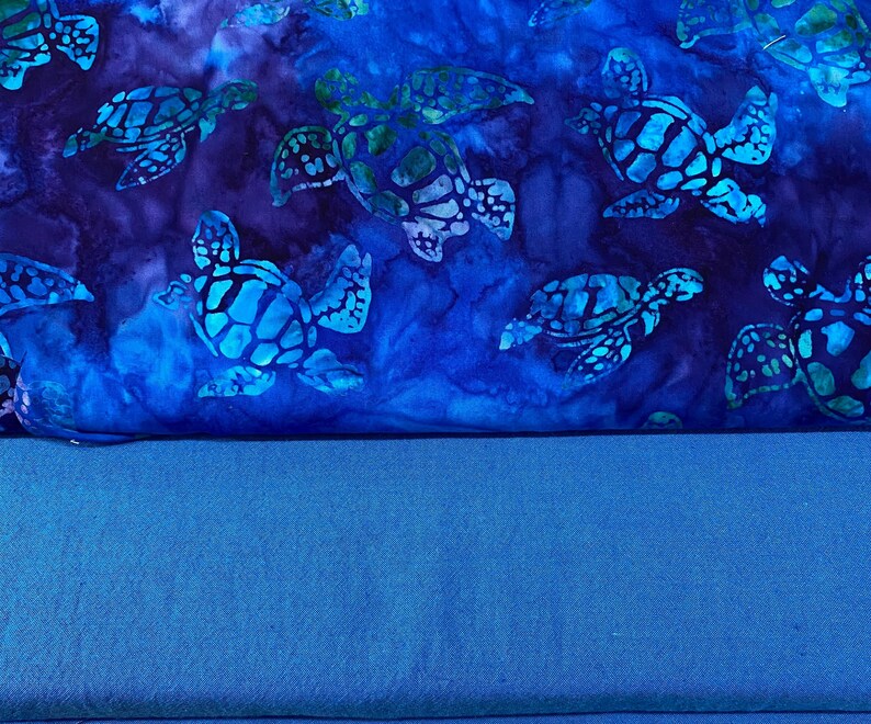 May include: A fabric with a blue and teal sea turtle pattern. The turtles have a detailed shell design and are set against a dark blue background with lighter blue accents. The bottom portion of the image is a solid blue fabric.