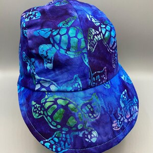 May include: A blue baseball cap with a sea turtle pattern. The cap features a vibrant design of turquoise and green sea turtles on a dark blue background. The brim is curved and the cap is made of fabric.