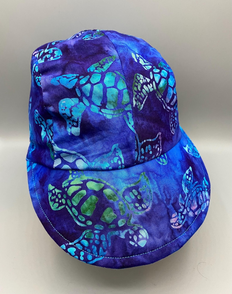 May include: A blue baseball cap with a sea turtle pattern. The cap features a vibrant design of turquoise and green sea turtles on a dark blue background. The brim is curved and the cap is made of fabric.