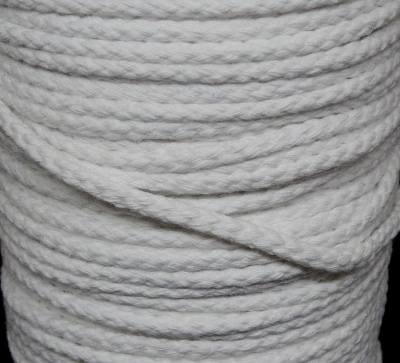 May include: A close-up of a spool of white cotton rope. The rope is tightly wound and has a braided texture.