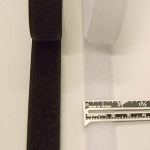 May include: A black and a white strip of hook and loop fastener tape positioned side by side. A metal ruler is placed across the white strip, showing a width of approximately 0.75 inches for the fastener tape material.
