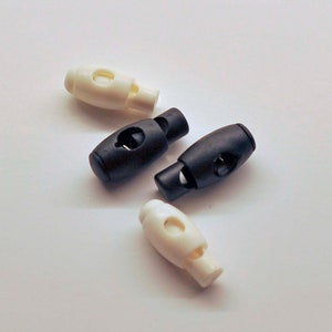 May include: Four plastic cord stoppers, two white and two black. The stoppers have a small hole in the center and a larger hole on the side.