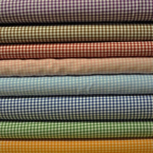 May include: A stack of eight gingham fabric rolls in various colors, including purple, brown, red, pink, light blue, dark blue, green, and orange.