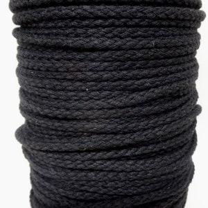 May include: A close-up of a spool of black cotton rope. The rope is tightly wound and has a rough texture.